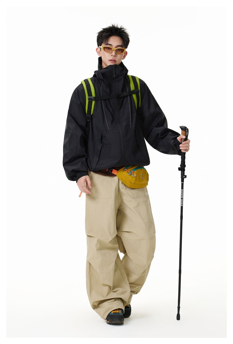 Model wearing a black high-collar jacket with beige trousers and a lime-accented backpack.
