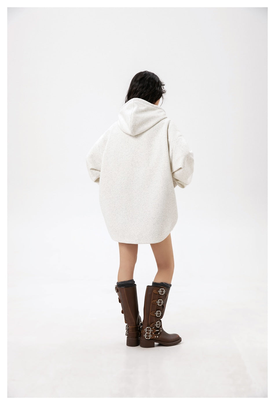 Rear view of a model wearing an oversized light gray hooded sweatshirt with a plain back.