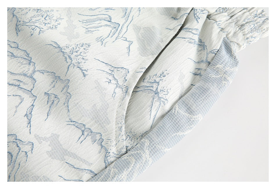 Close-up of a seam and folded edge on white shorts with a pale blue landscape print.