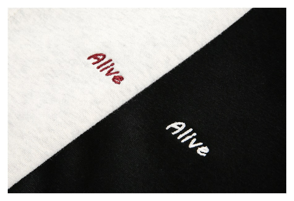 Close-up of off-white and black garment fabric, each embroidered with the word “alive.”