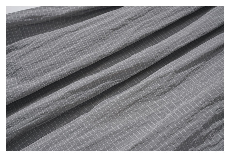 Close-up of gray trousers with a fine white grid pattern and soft folds.