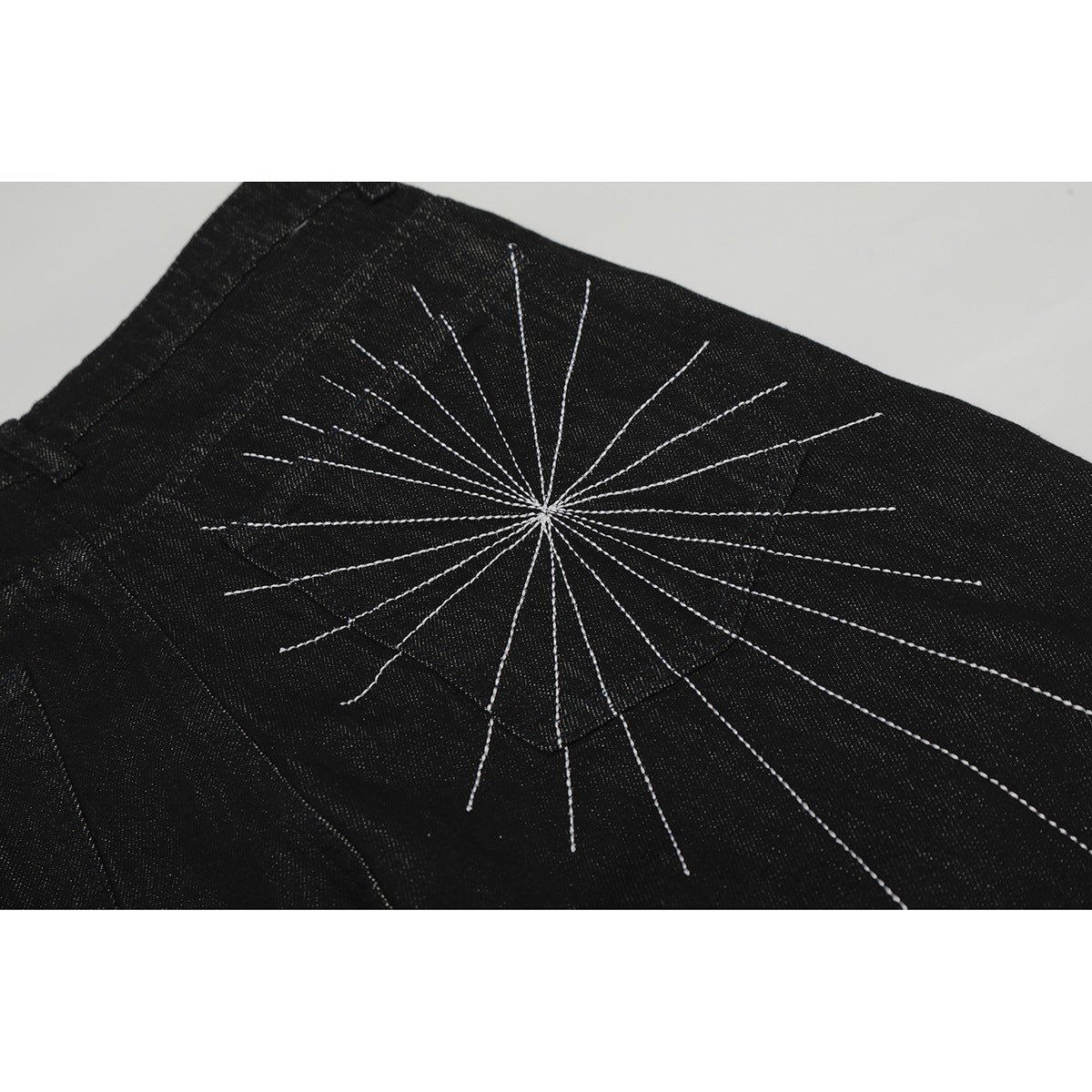 Close-up of black jeans with a large white radiating stitched motif across the back pocket area.