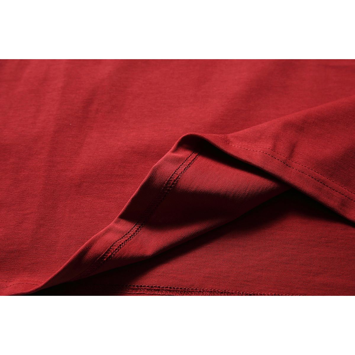 Close-up of the red T-shirt fabric folded to show its stitched hem and seam.