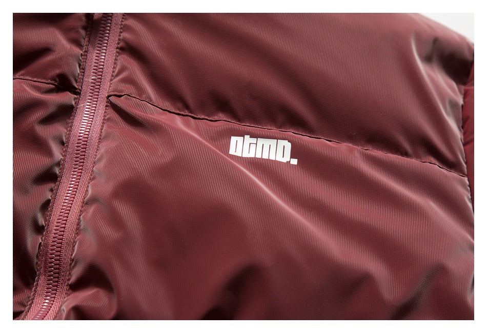 Close-up of a burgundy quilted jacket with a white logo printed on the chest.