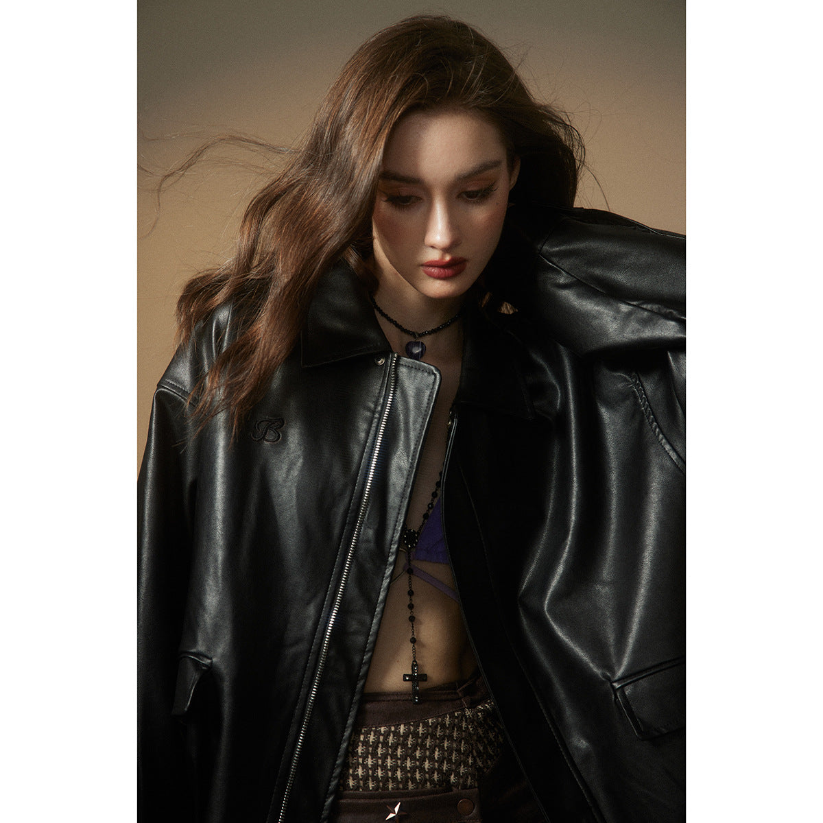 Close view of a black leather-look jacket's wide lapels, zip front and small embroidered chest emblem.