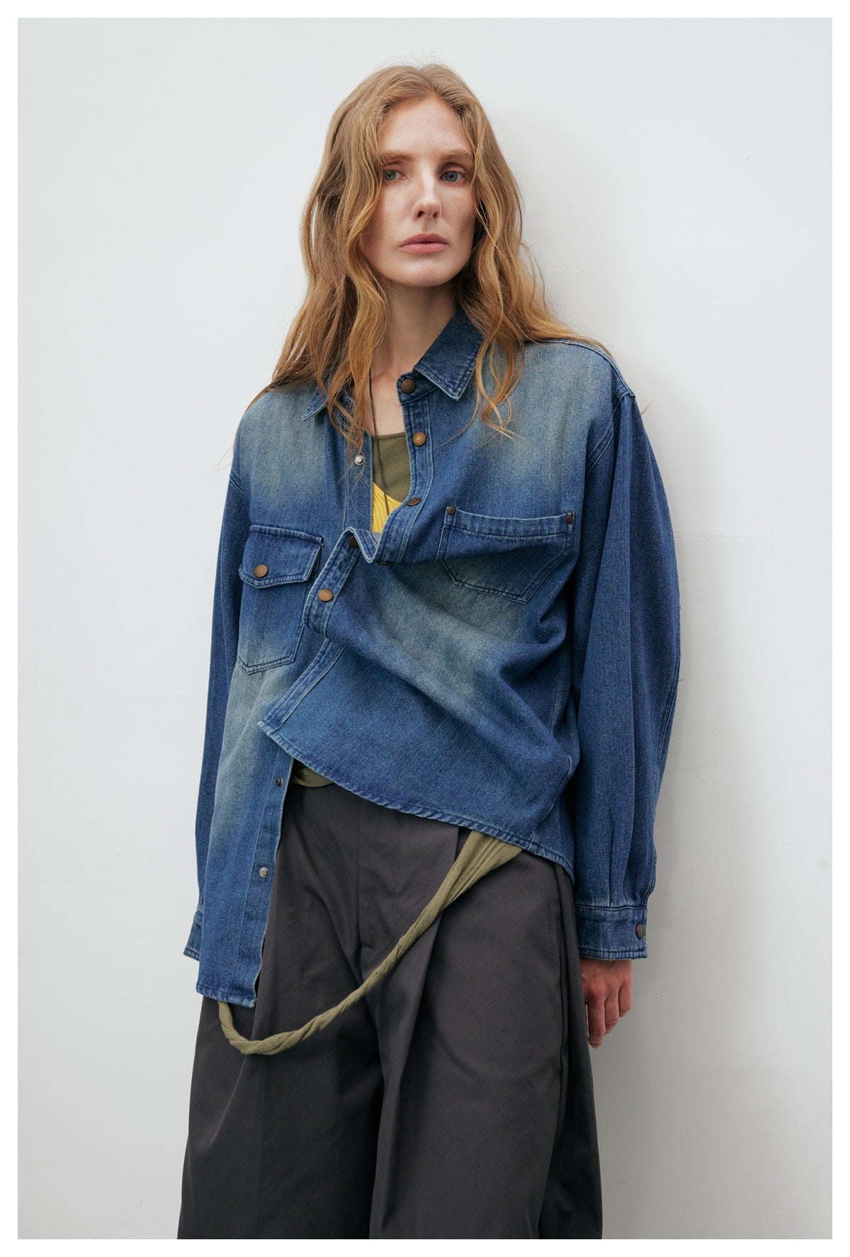 Model showing the front of a blue denim shirt jacket, with one sleeve folded across the body.