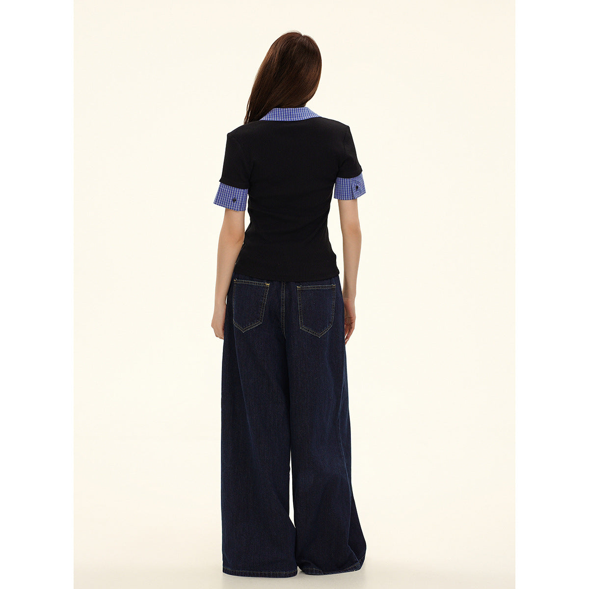 Back view of a model wearing a black polo with a blue check collar and sleeve cuffs, and dark wide-leg jeans.