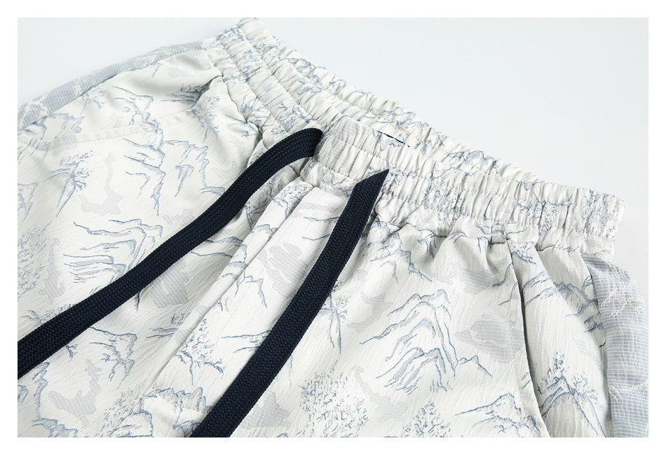 Close-up of the elastic waistband and navy drawstrings on white shorts with a pale blue landscape print.