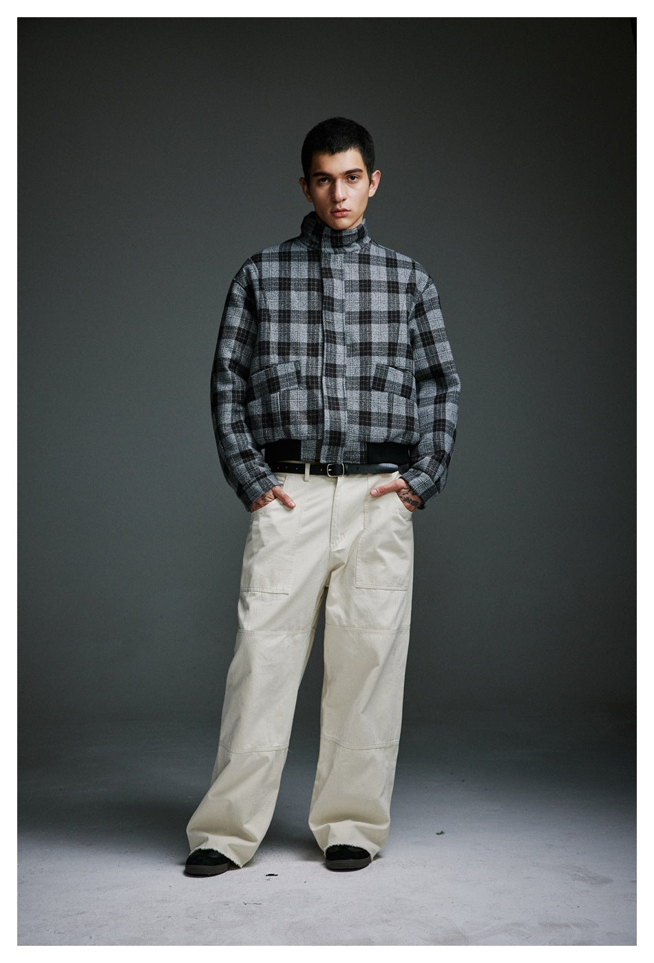 Full-length view of a man wearing a gray and black plaid jacket with cream cargo pants.
