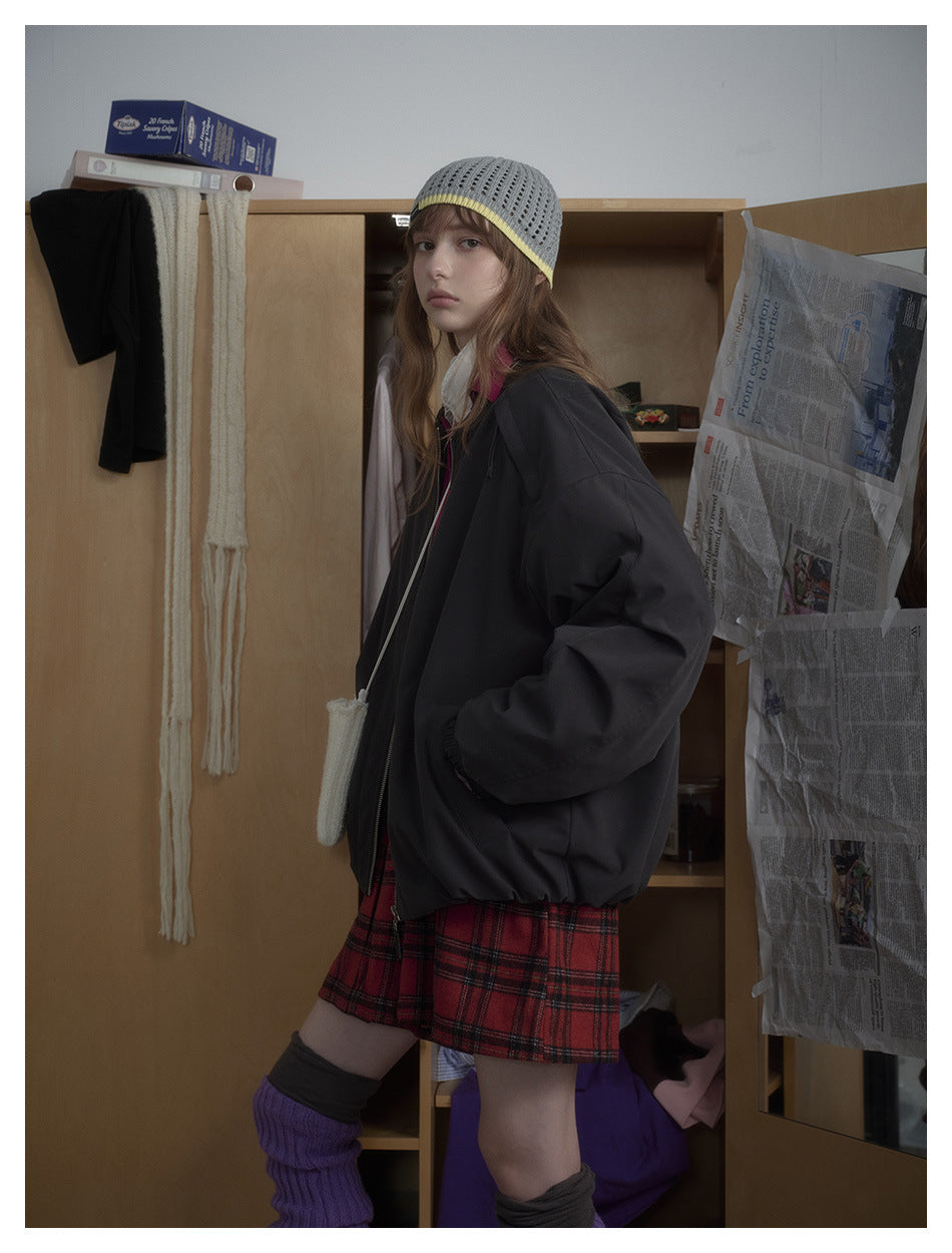 Three-quarter side view of a model wearing an oversized black zip-front bomber jacket and red plaid shorts.