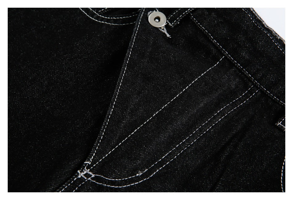 Close-up of black jeans showing a metal button and curved fly seam with white stitching.