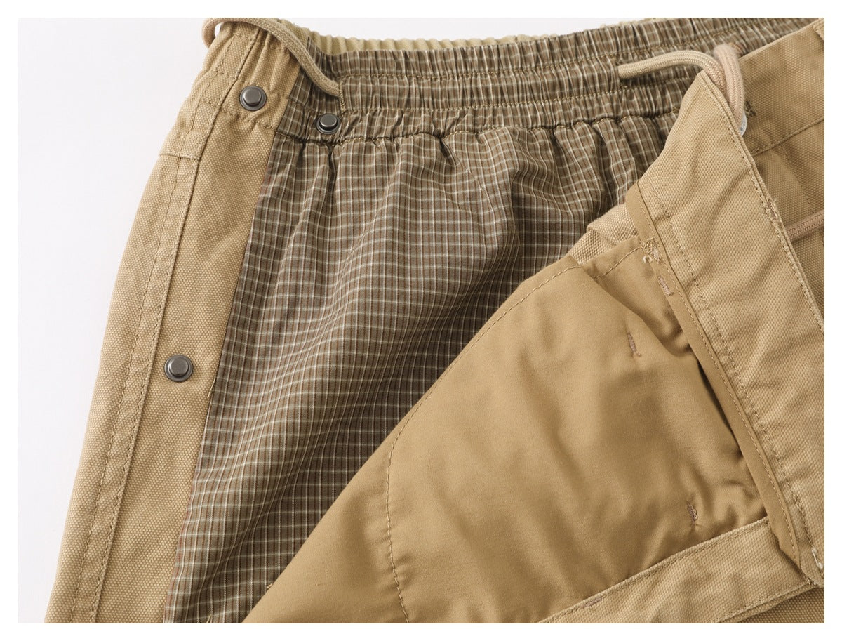 Close-up showing the tan pants' elastic waist, snap fastening, and brown plaid inner lining.