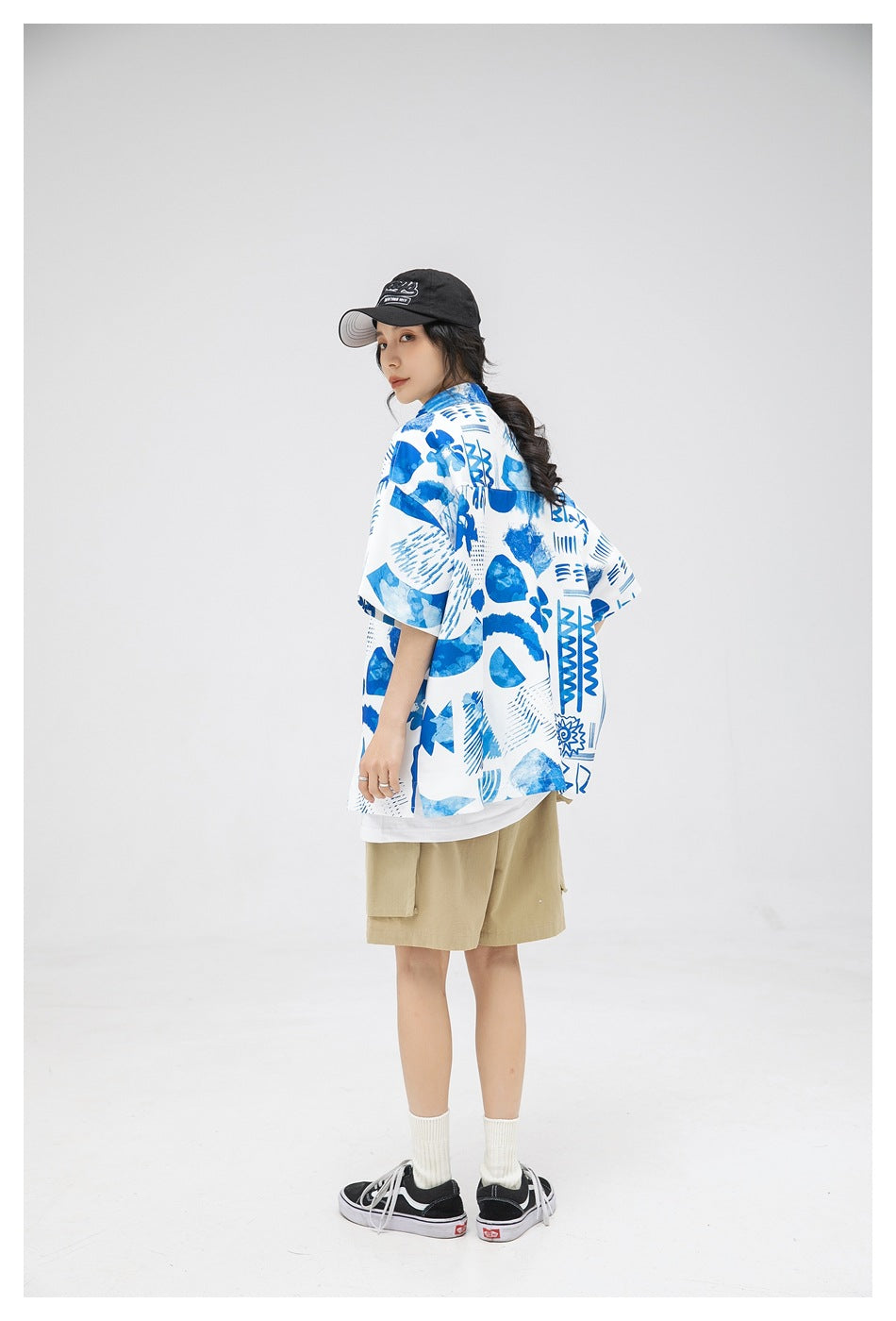 Model wearing a white and blue abstract-print shirt and khaki shorts, turned to show the shirt from the back at an angle.