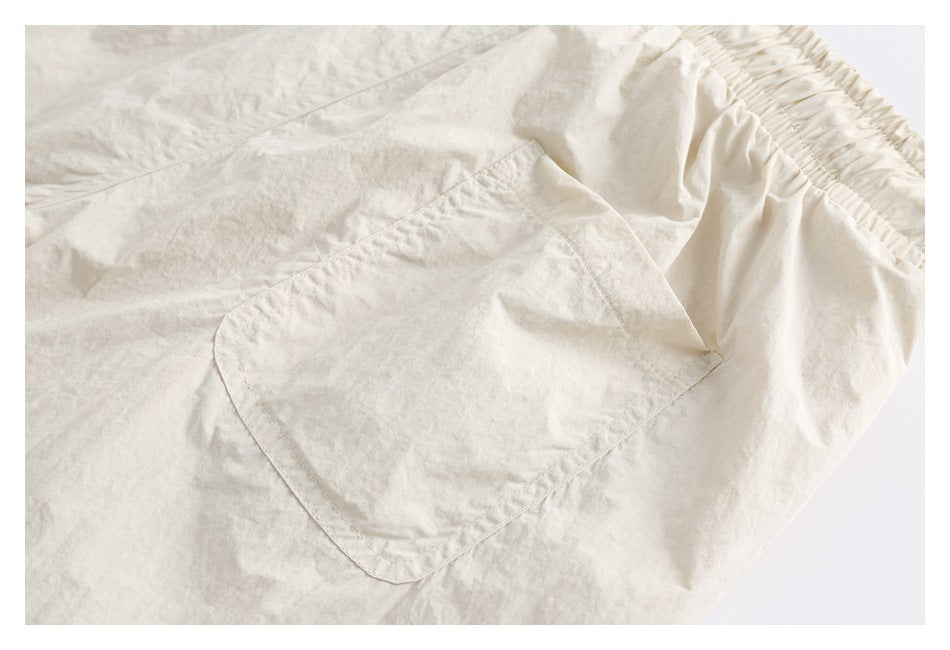 Close-up of a light cream garment showing a stitched patch pocket and gathered elastic waistband.
