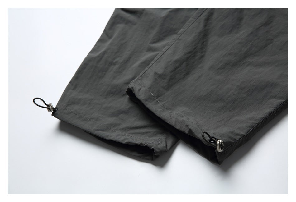 Close-up of charcoal pant hems with adjustable cord loops and metal toggles.