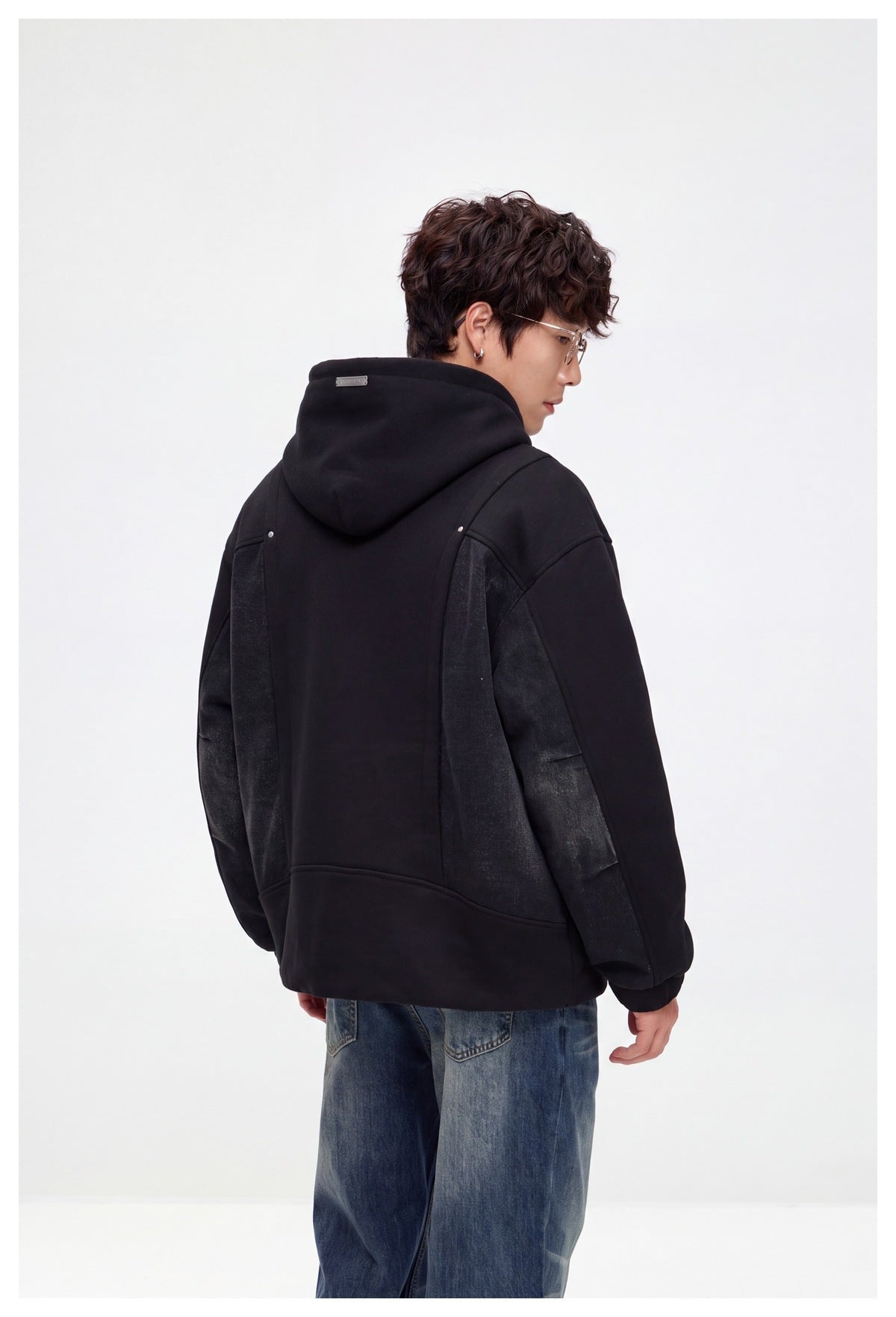 Back view of a model wearing a black hooded jacket with dark denim side and sleeve panels.