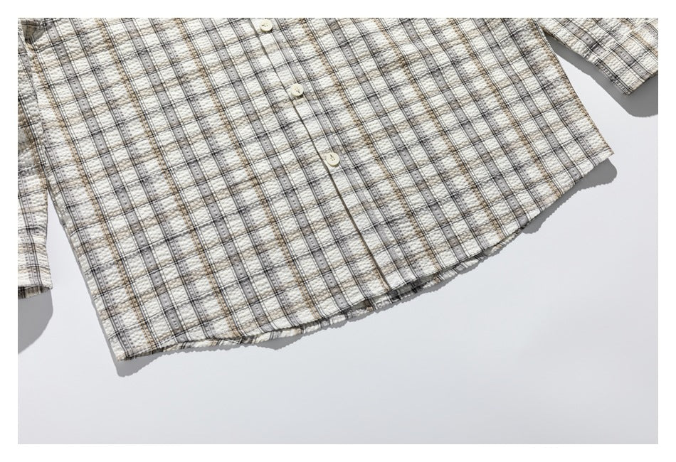 Partial flat-lay view of a cream plaid button-up shirt, showing its buttons and lower front hem.