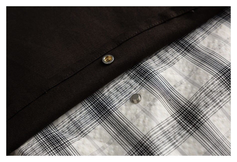 Close-up of metal snap fasteners along the dark jacket panel beside cream and black plaid fabric.