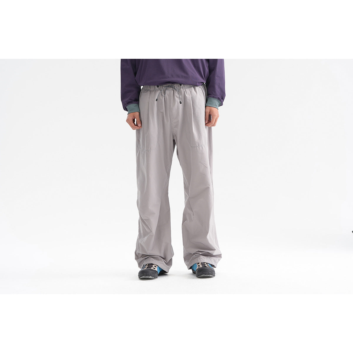Front view of a model wearing loose gray trousers with a drawstring waist and dark hiking shoes.
