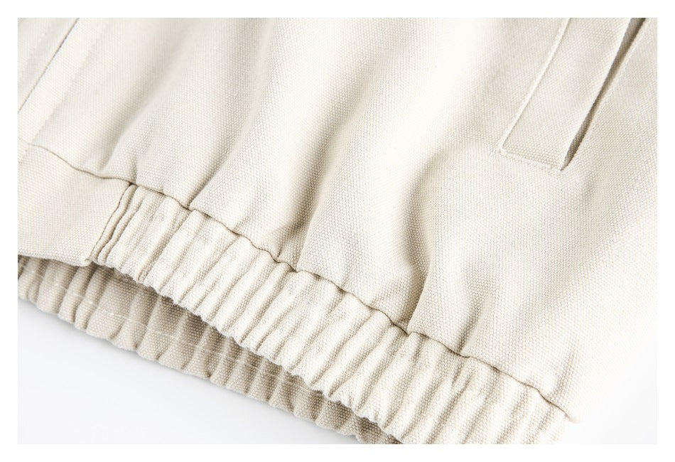 Close-up of cream garment fabric with a welt pocket and gathered elastic waistband.