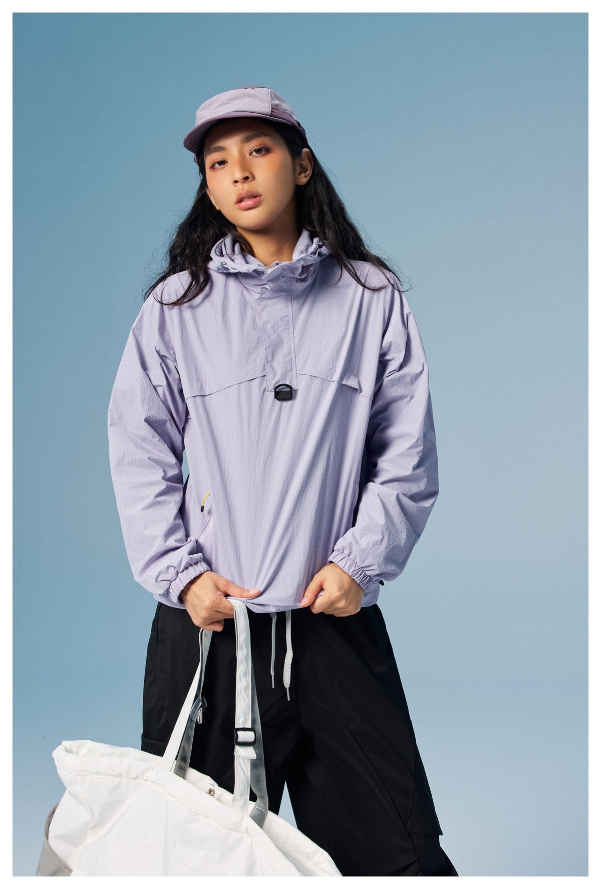 Front view of a model wearing a light lavender hooded pullover, black pants, and a matching cap.