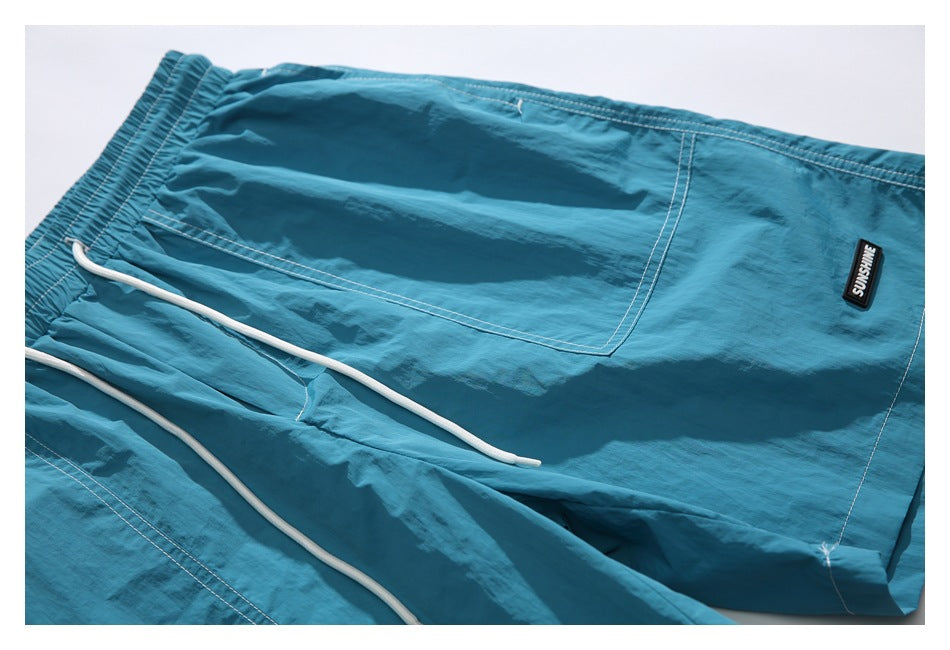 Teal shorts laid flat, showing the elastic drawstring waist, white drawcords, and front pocket.