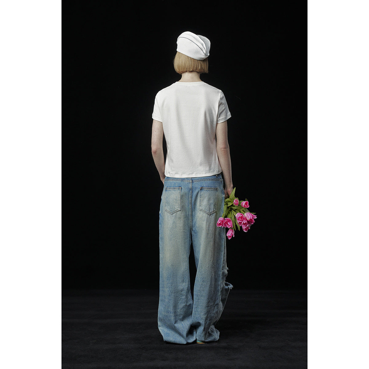 Rear view of a model wearing a plain white T-shirt and oversized light-blue jeans with back pockets.