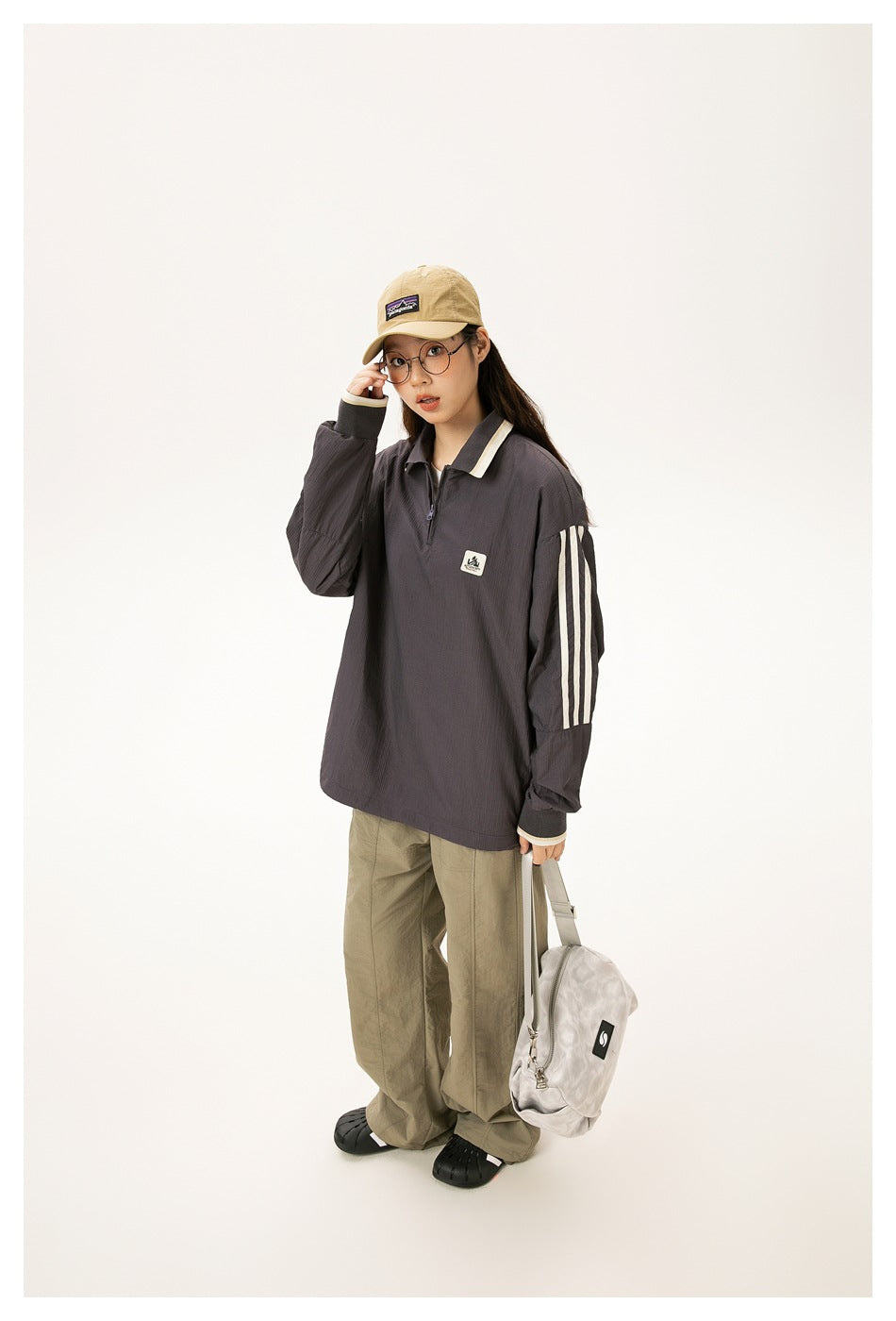Model wears a charcoal oversized quarter-zip pullover with cream collar trim and three cream stripes down the sleeves.