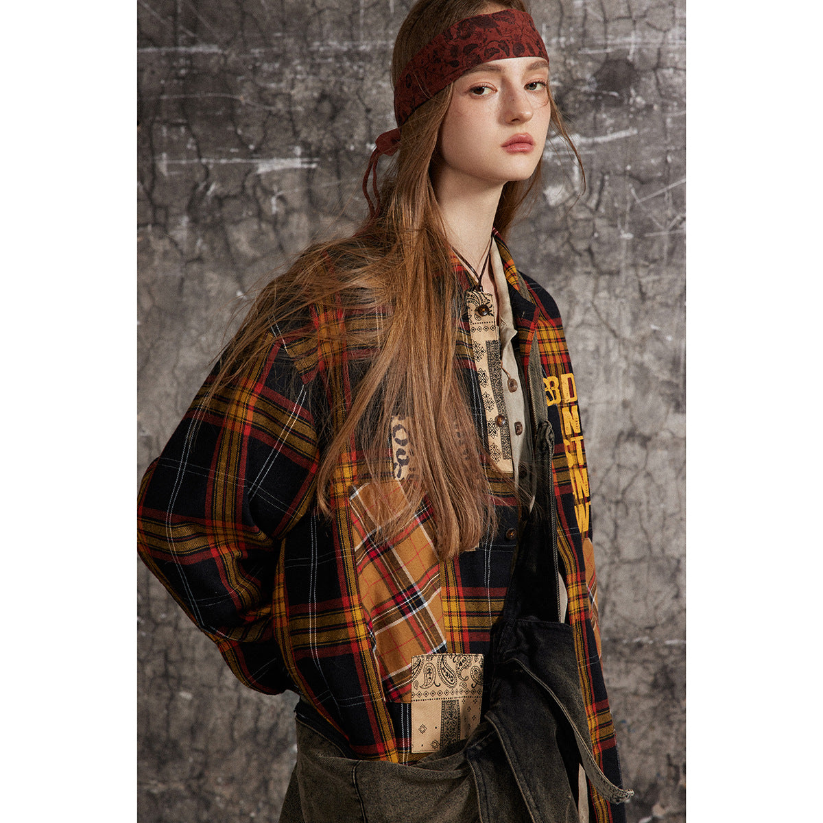 Model wearing an oversized black, red and mustard plaid shirt-jacket with patchwork panels and yellow lettering.