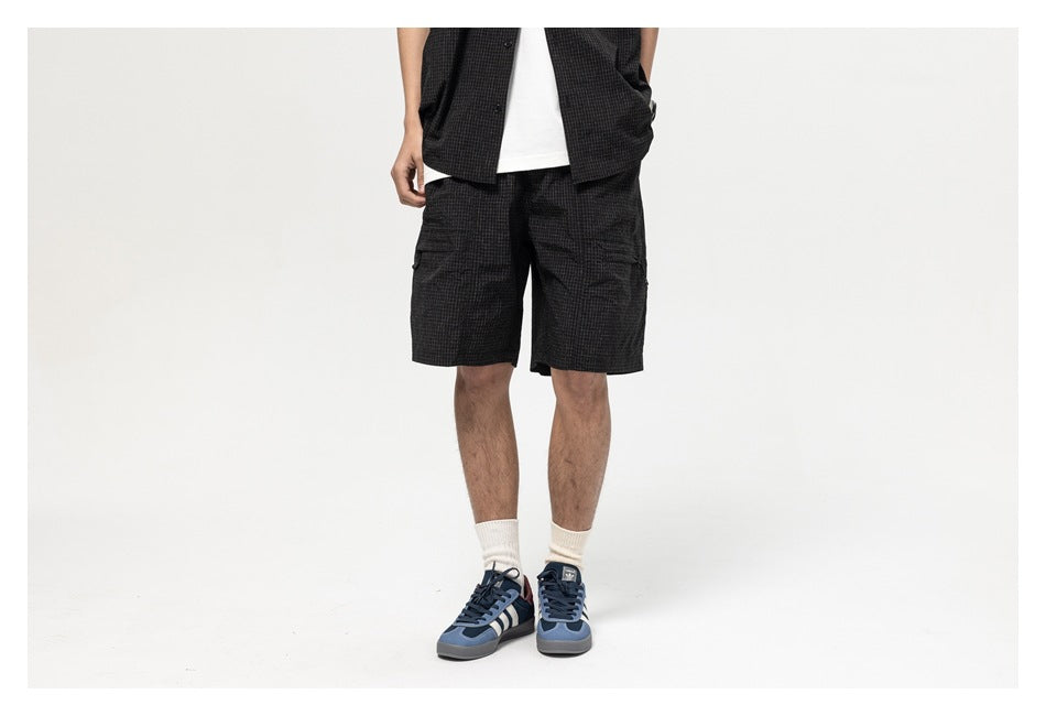 Front view of a model wearing black grid-pattern shorts with side zip pockets, white socks and blue sneakers