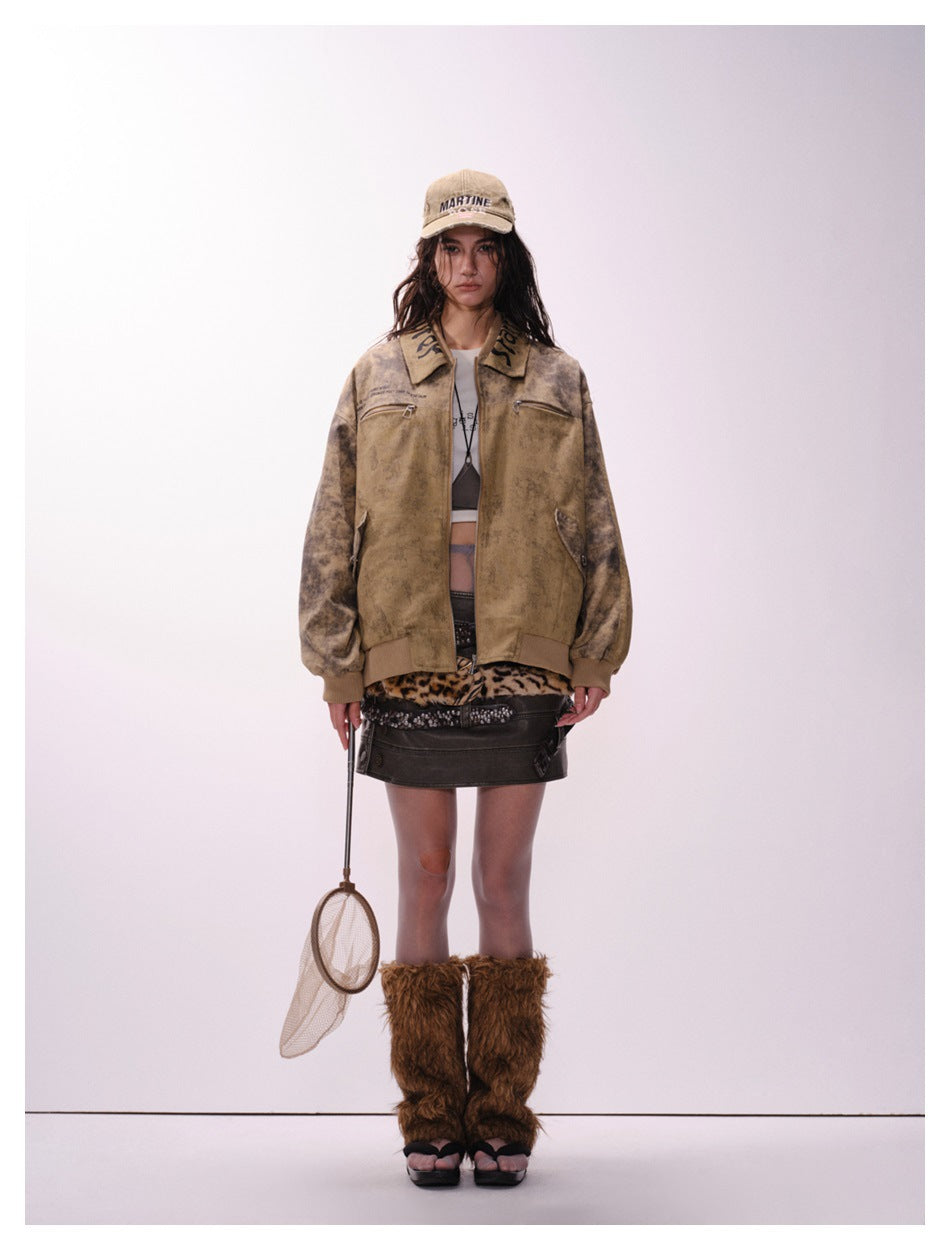 Model wearing the brown mud-dyed zip jacket open, front view, with a cap, dark mini skirt and fur leg warmers