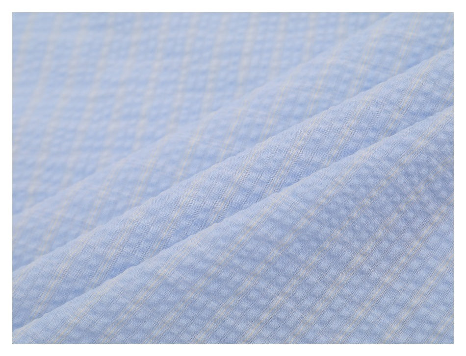 Close-up showing the subtle woven check pattern and texture of light blue shirt fabric.
