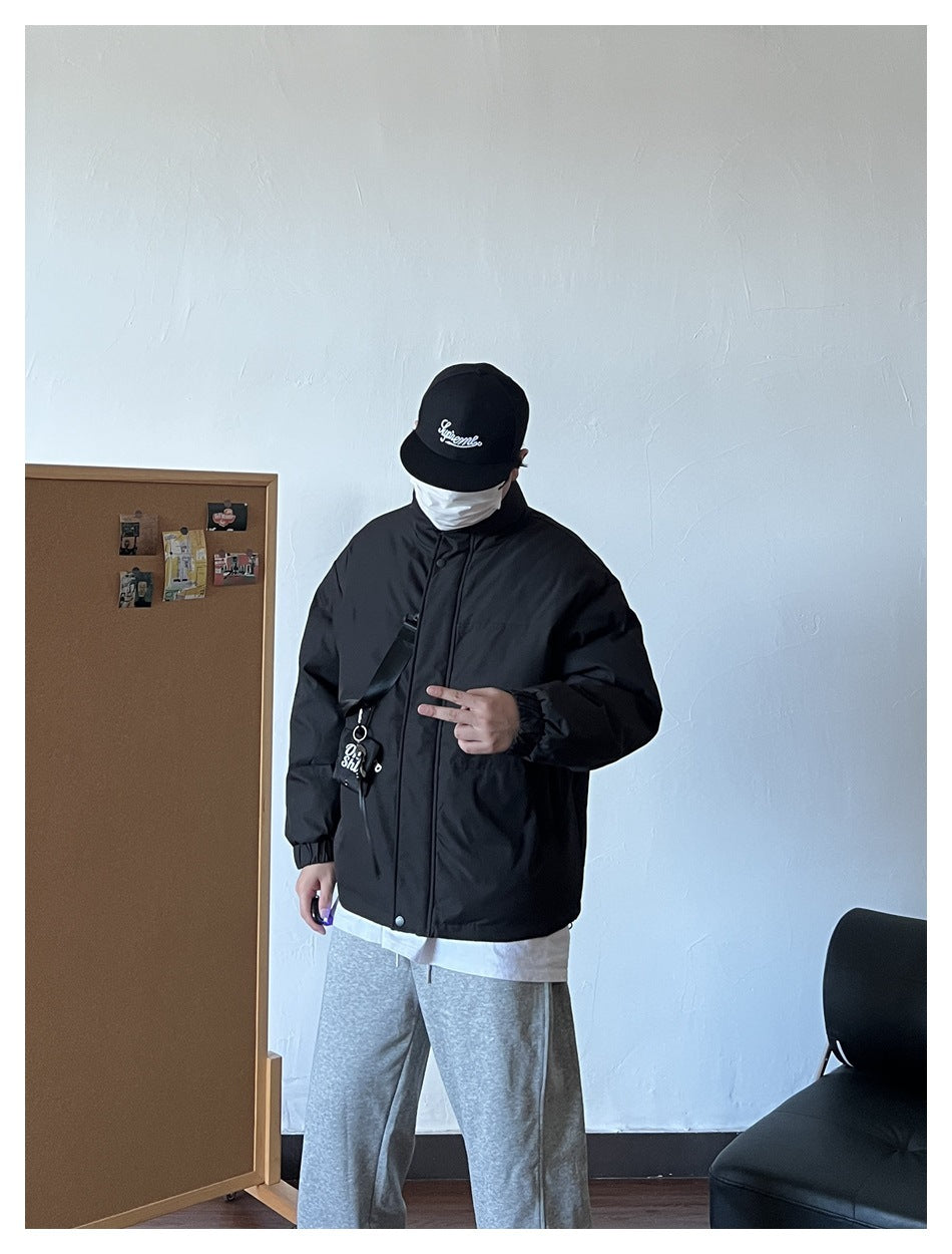 Person wearing black puffer jacket with front strap and pouch, gray sweatpants and black cap, front view