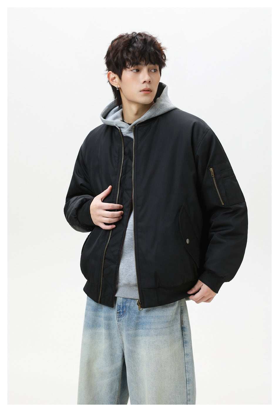 Model in black bomber jacket with sleeve zip pocket, gray hoodie and light-wash jeans, angled view