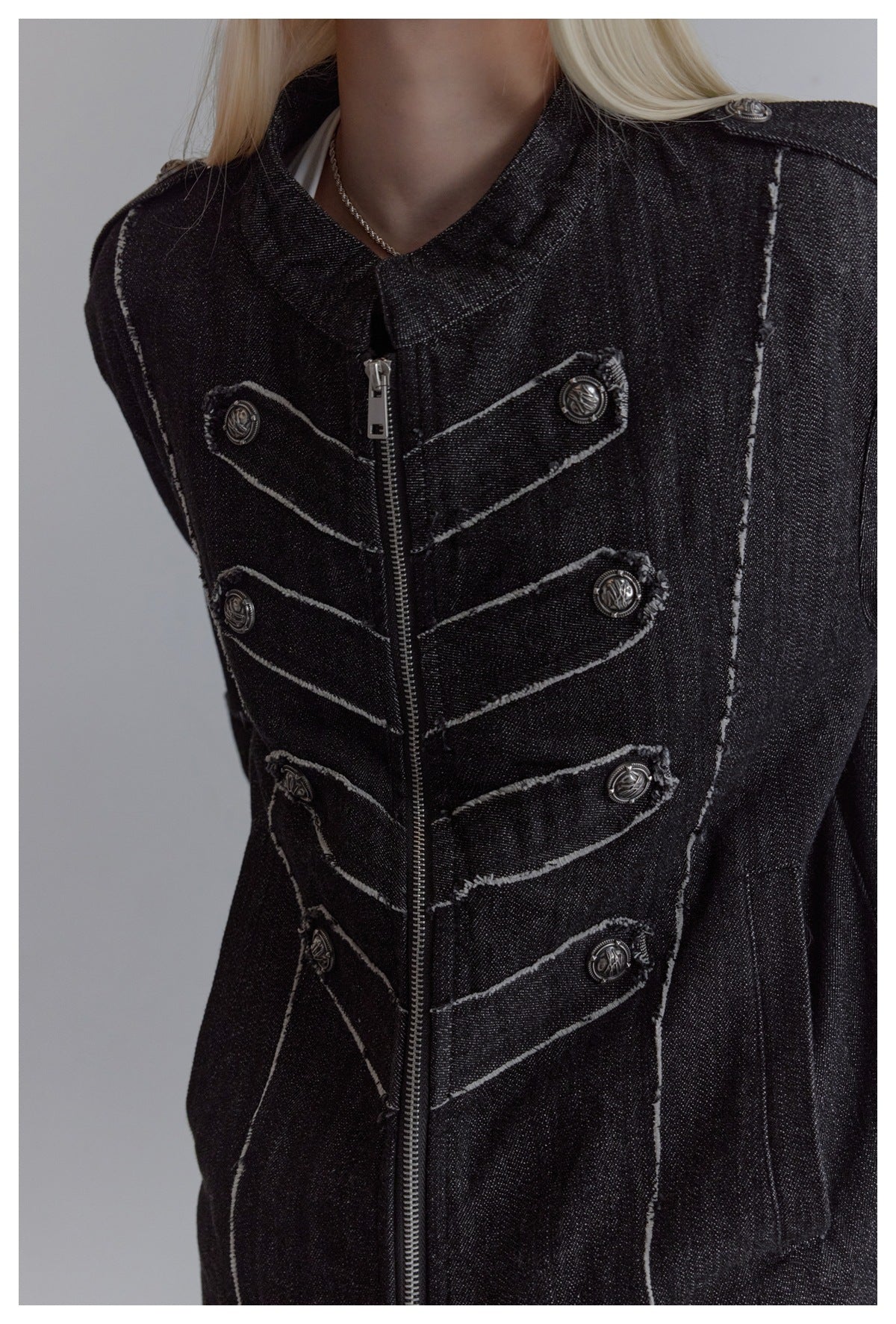 Close-up of a black jacket's zip front, raised decorative buttons, contrast stitching and shoulder tabs.