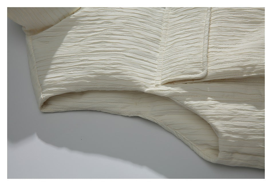 Close-up of the ivory vest's armhole, pocket edge, and rippled fabric texture.