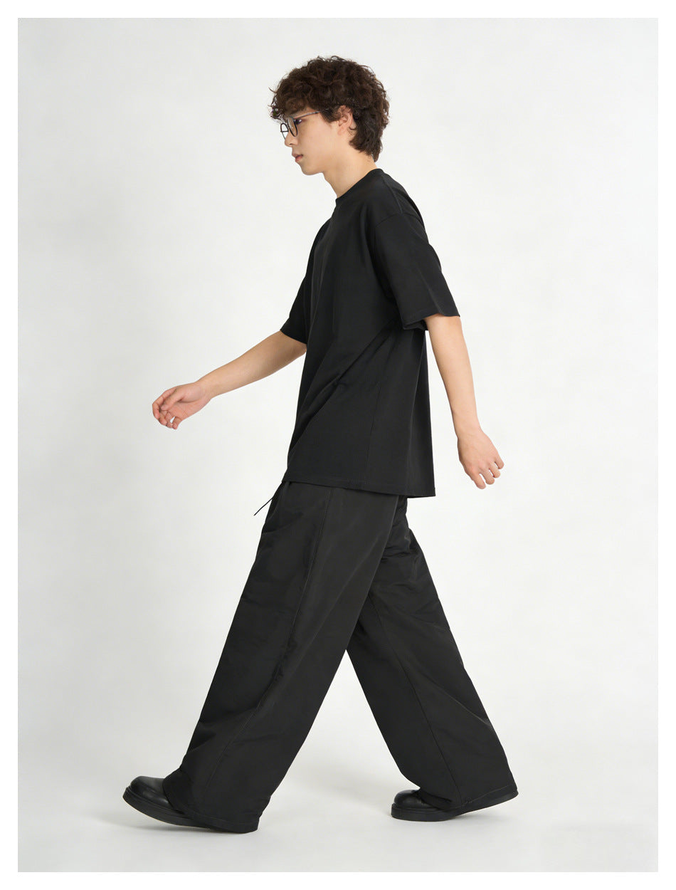 Side view of a model walking in a black oversized T-shirt and loose black trousers.
