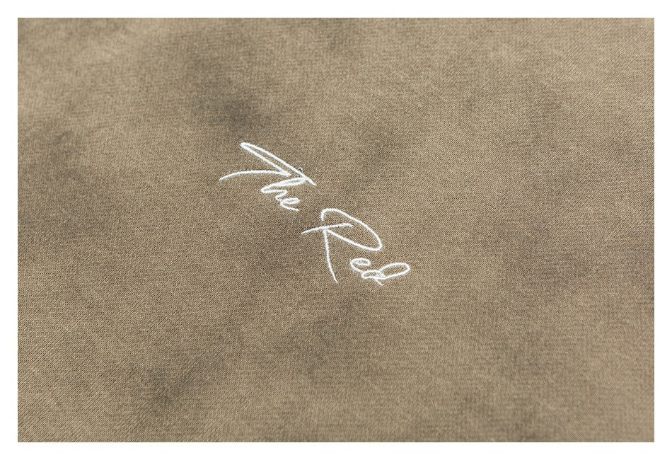 Close-up of white “The Red” script embroidery on mottled tan-brown sweatshirt fabric.