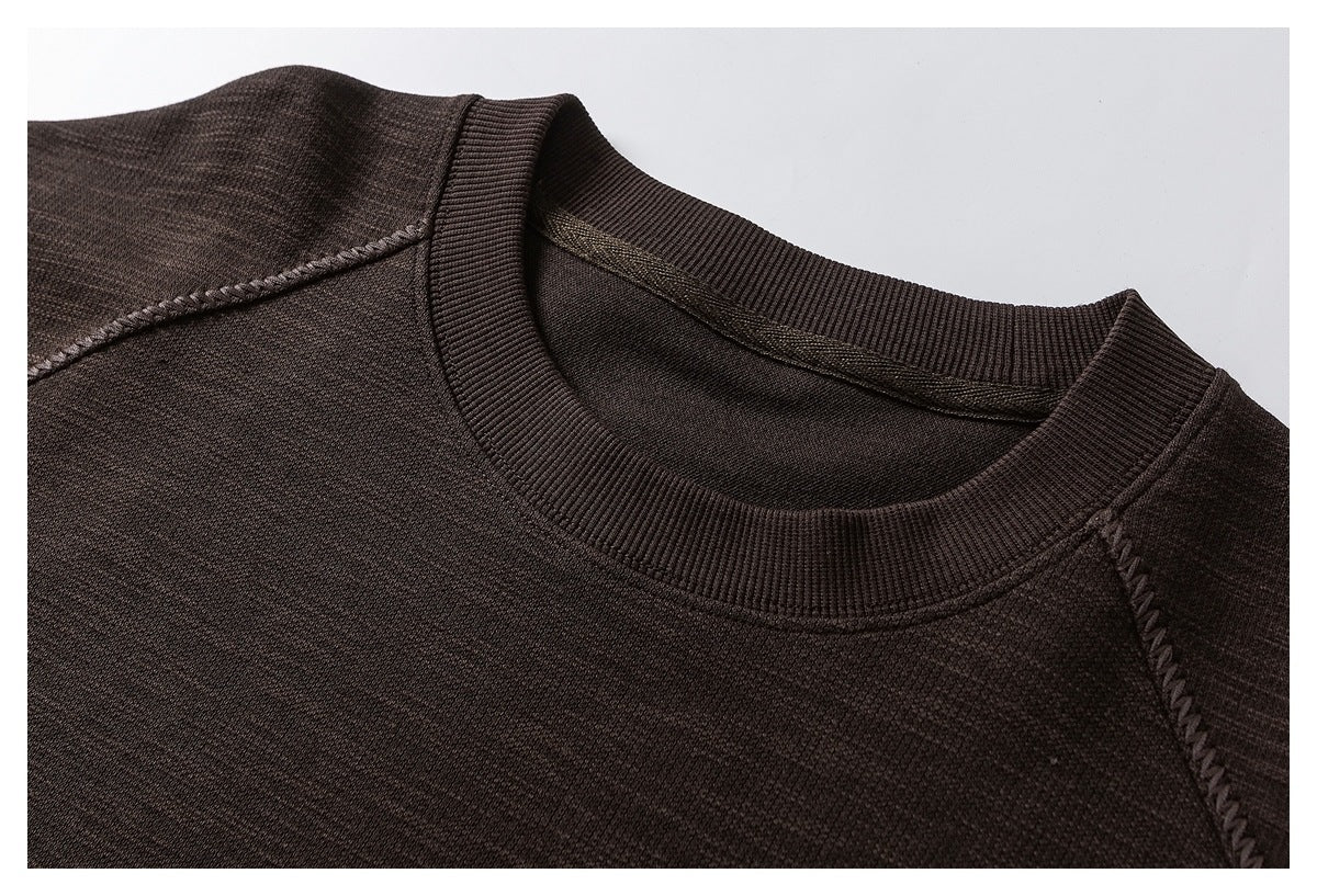 Close-up of a dark brown sweatshirt's ribbed crew neckline and raglan seam.