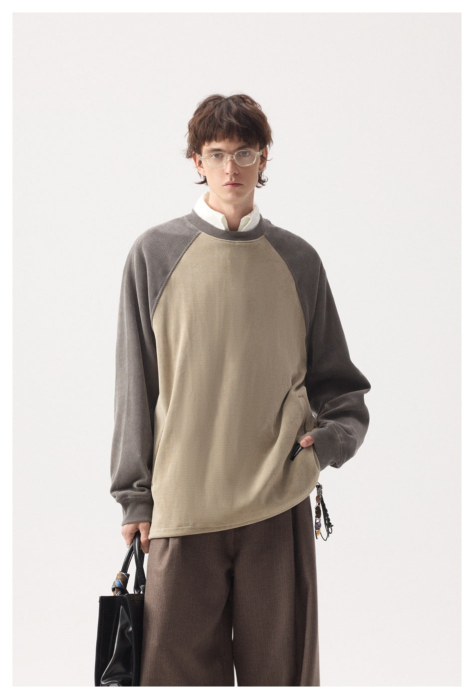 Model wearing a tan raglan crew-neck sweatshirt with taupe sleeves over a white collared shirt, hand in pocket
