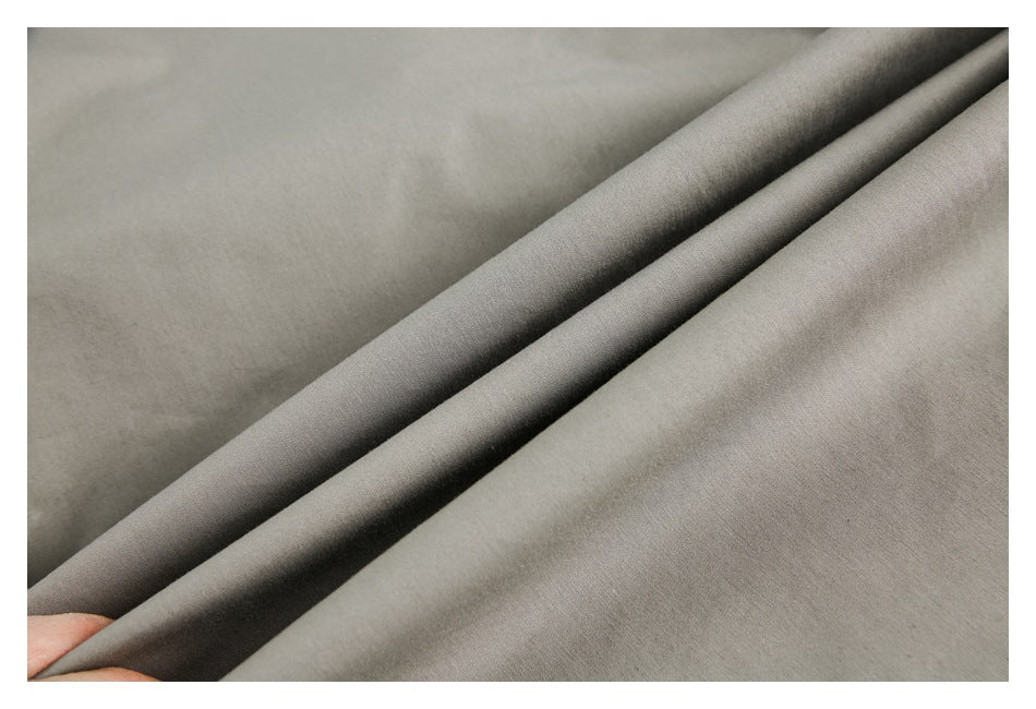 Close-up of gray fabric draped in folds, with a hand holding the edge.