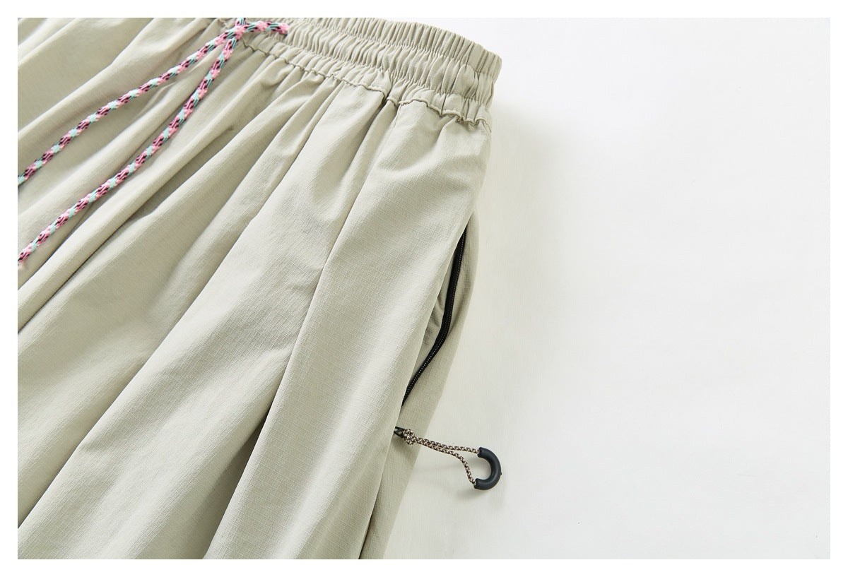 Close-up of pale khaki trousers showing the elastic waistband, pink patterned drawcord, and black side-adjustment toggle.