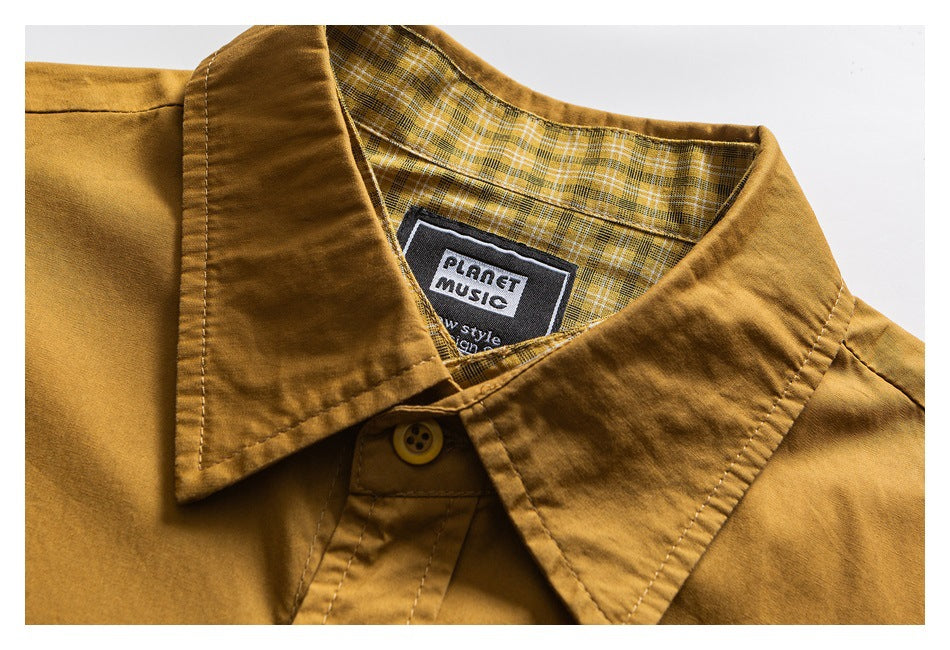 Close-up of a mustard shirt's pointed collar, plaid lining, button, and sewn neck label.