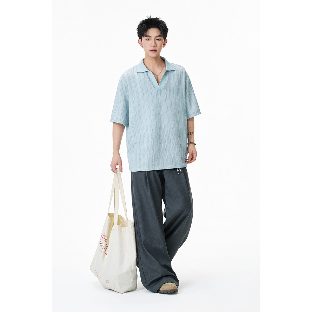 Model wearing a pale blue textured short-sleeve polo with dark wide-leg trousers.