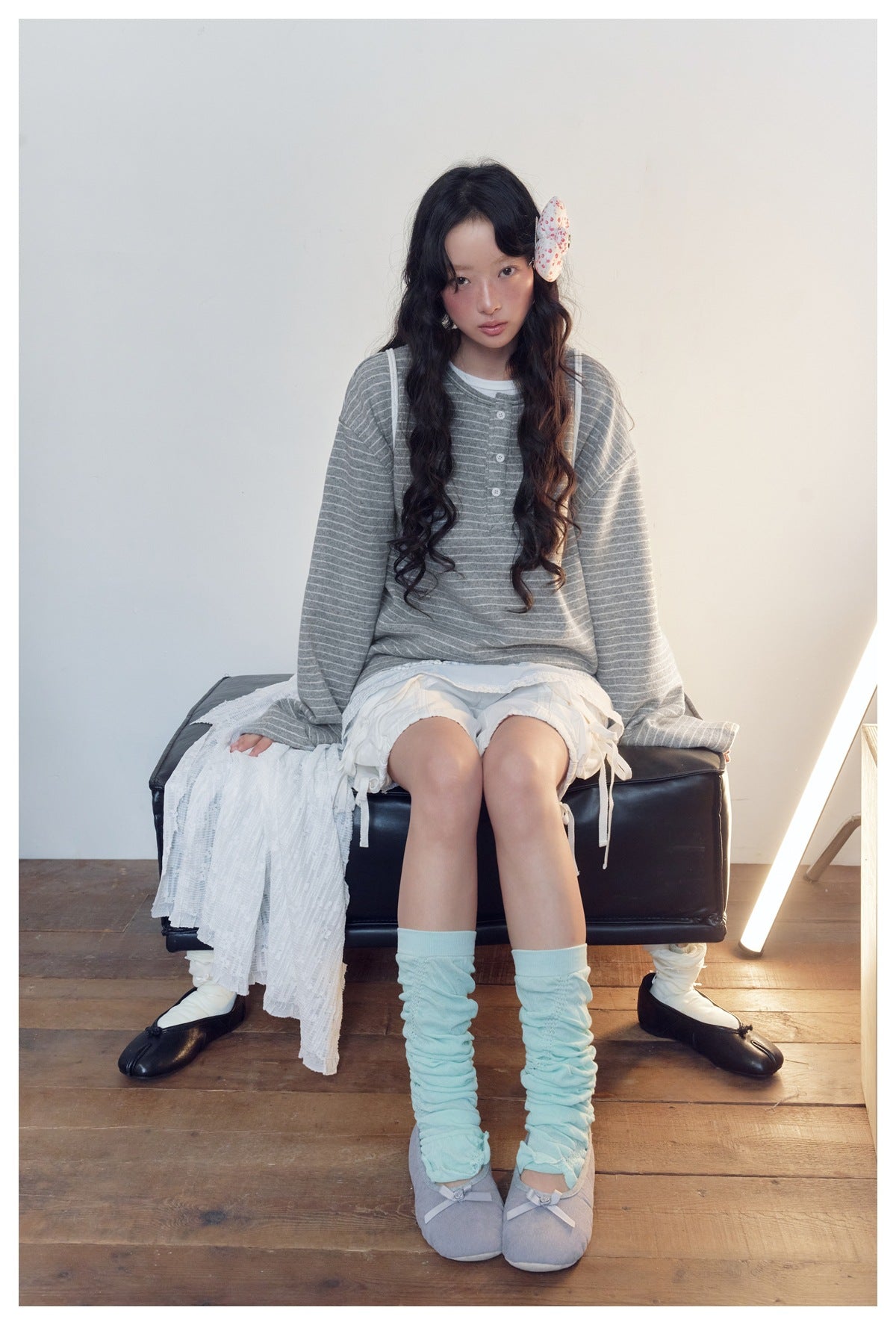 Seated model in a gray-and-white striped button-front top, pale blue layered skirt and white shorts.