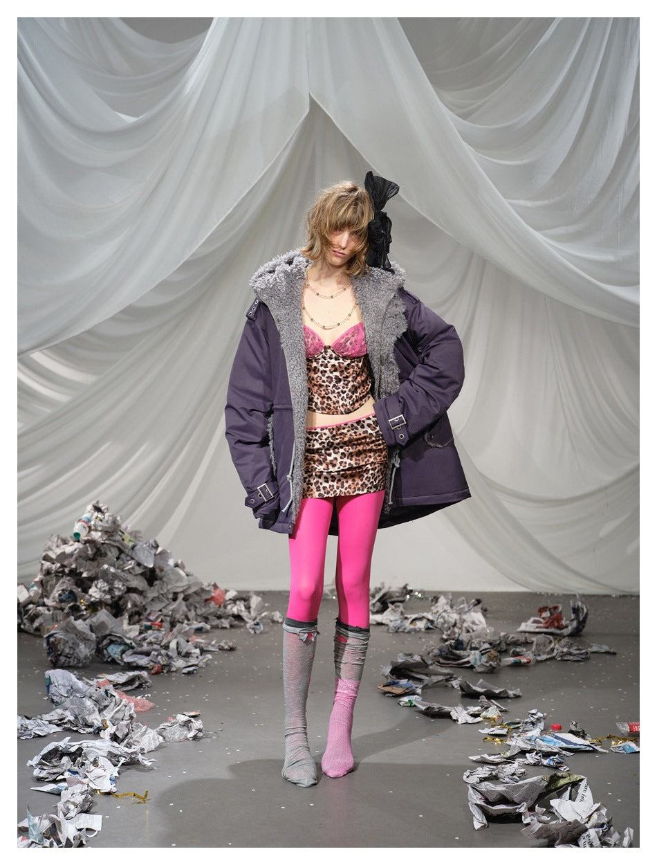 Model wearing an oversized plum parka with a shaggy gray collar over leopard-print clothing and bright pink tights.