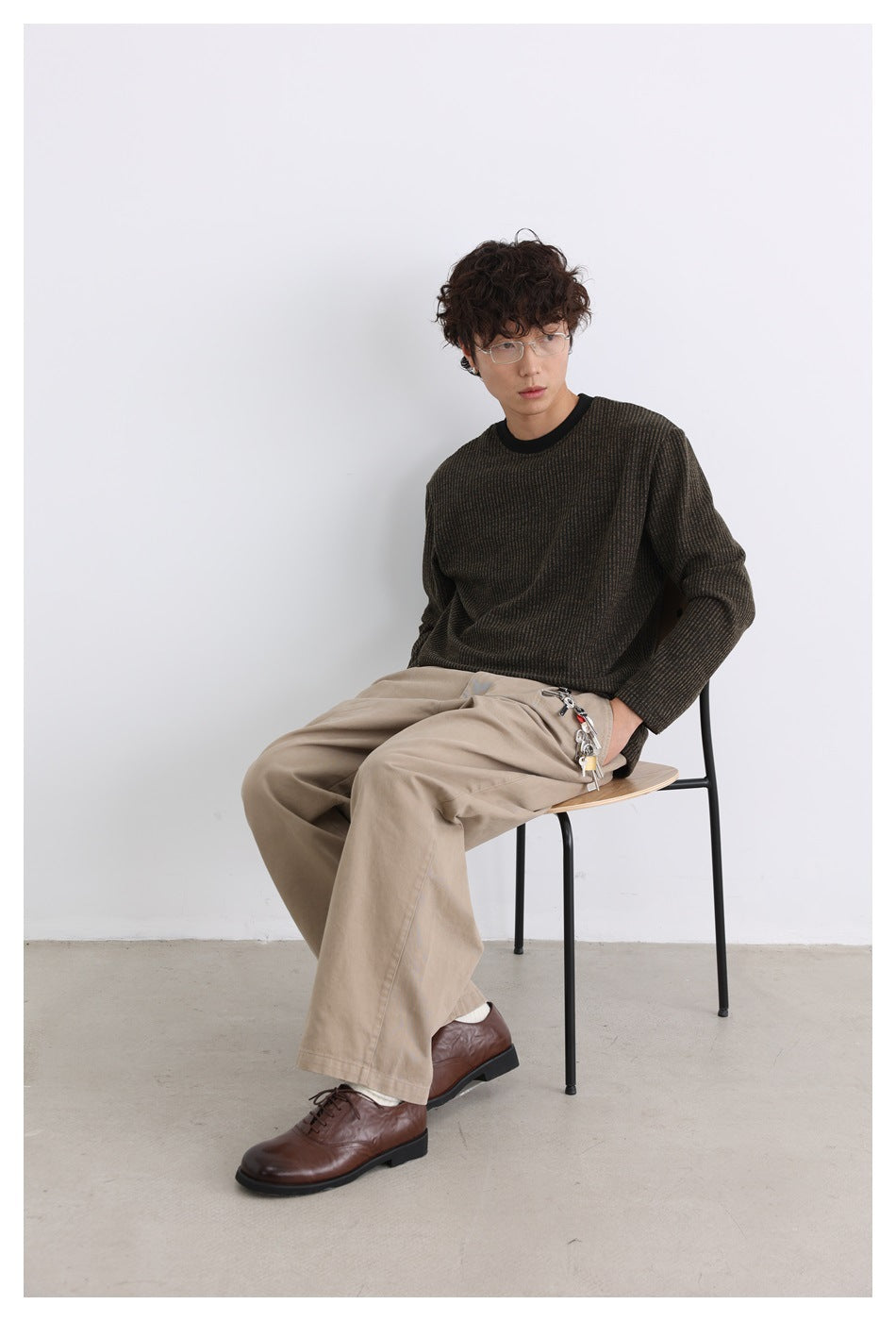 Seated model wearing a dark brown subtly striped long-sleeve shirt with a black crew neck.