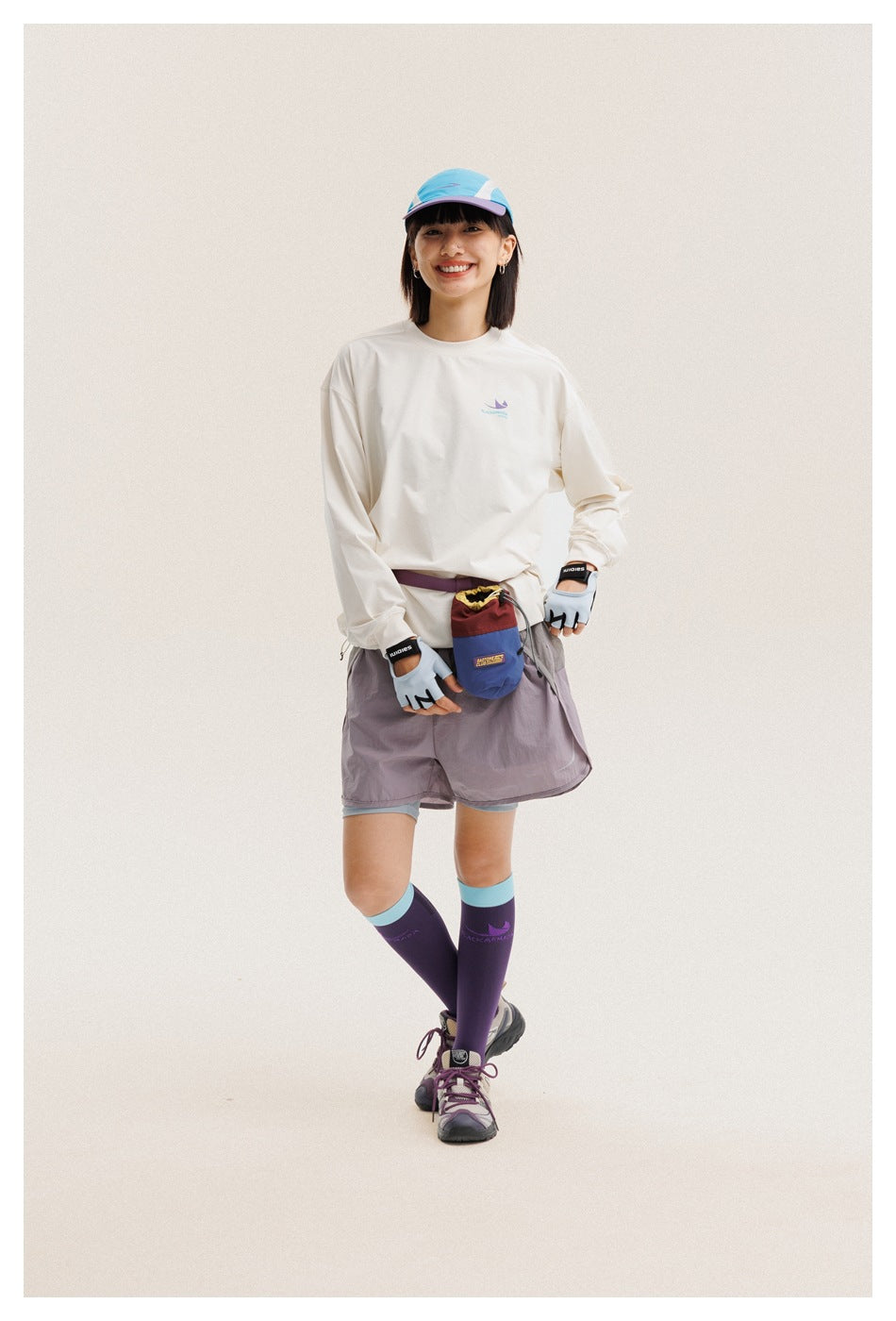 Full-length view of a model wearing a cream long-sleeve shirt, gray-mauve shorts, and purple knee socks.