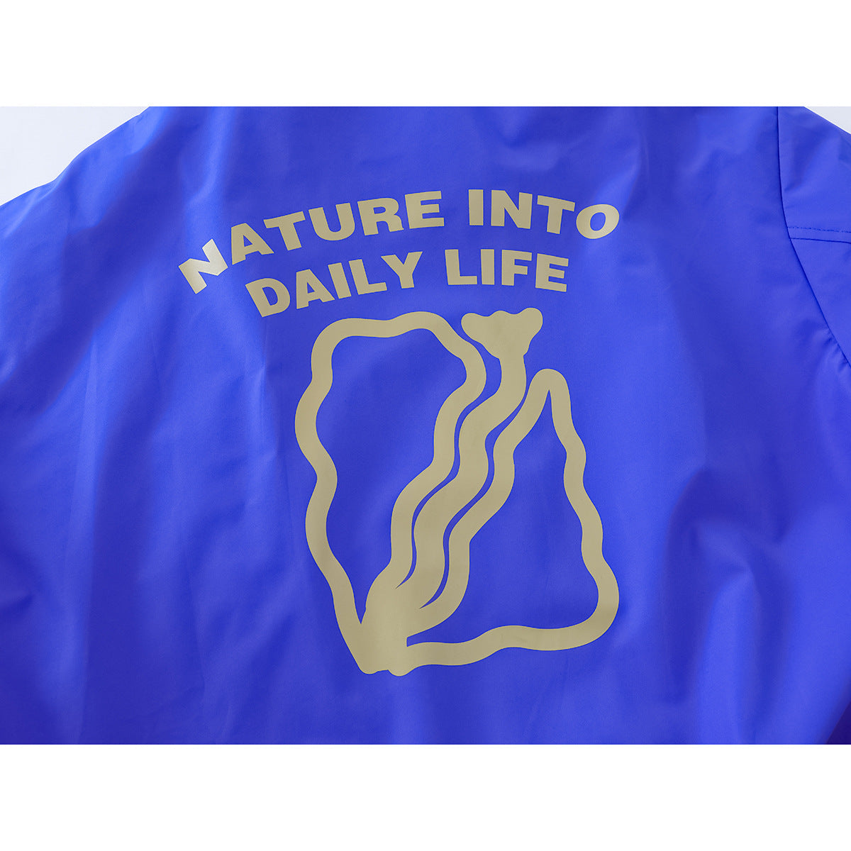 Back of a bright blue jacket with a large gold abstract graphic and the words “NATURE INTO DAILY LIFE.”