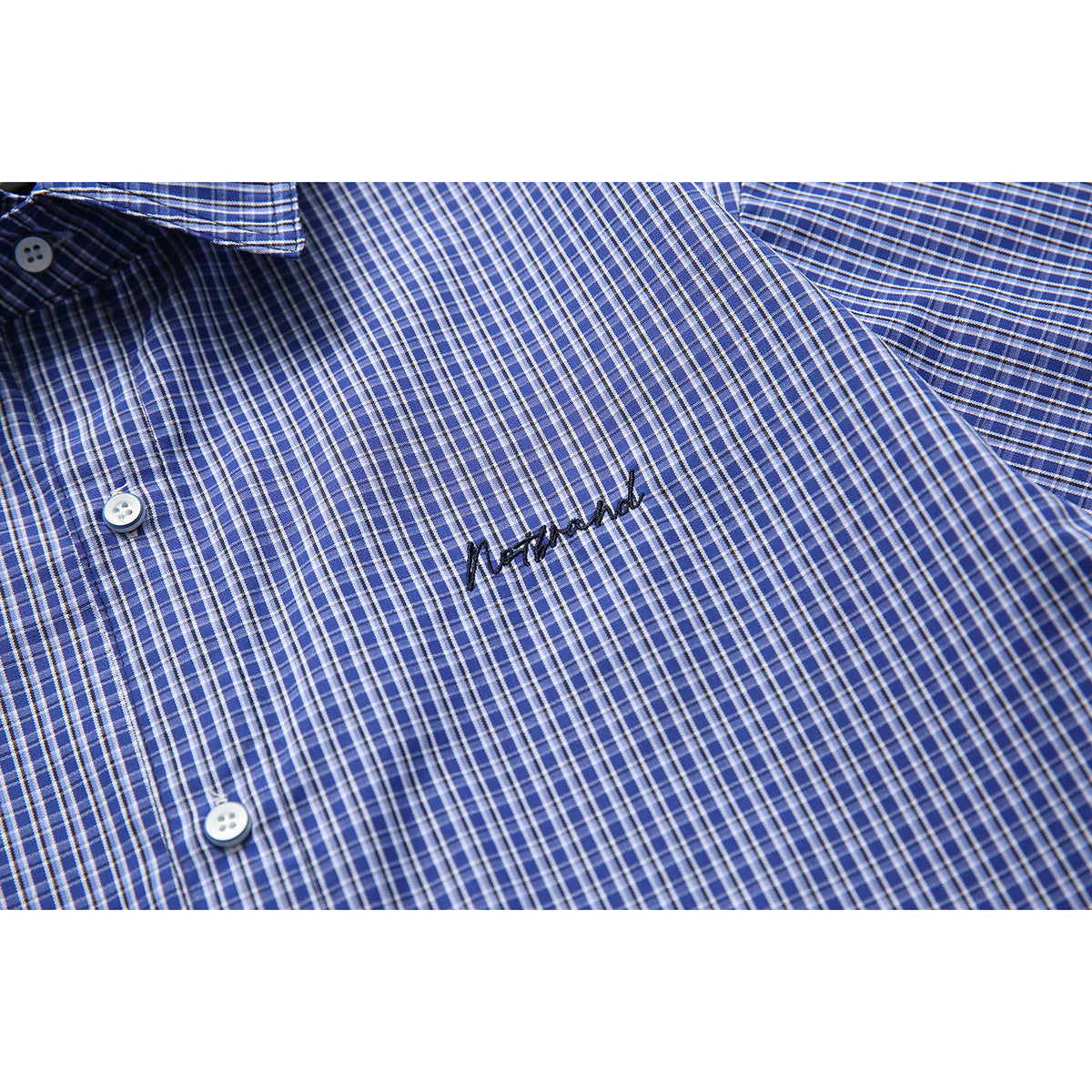 Close-up of a blue checked shirt front with white buttons and black embroidered script.
